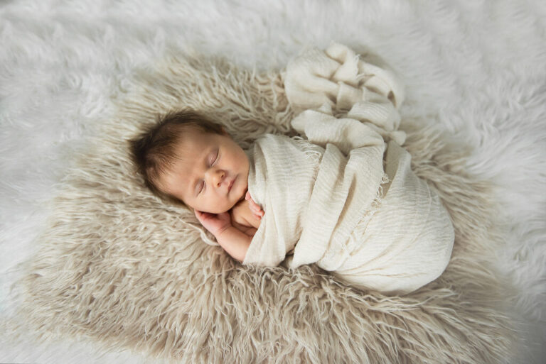Baby newborn on fur in cream wrap