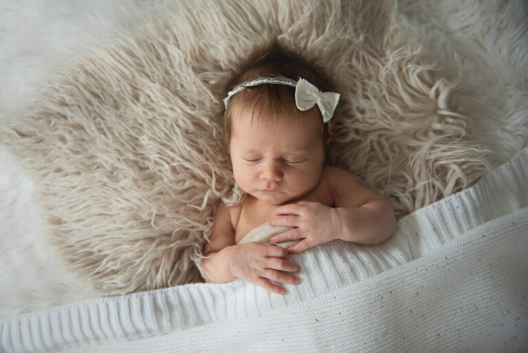 newborn baby girl sleeping on cream blanket with cream hair bow